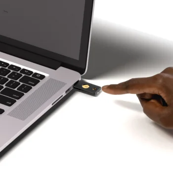 Security Key NFC insérée dans le port USB-A d'un ordinateur portable, doigt sur le bouton tactile